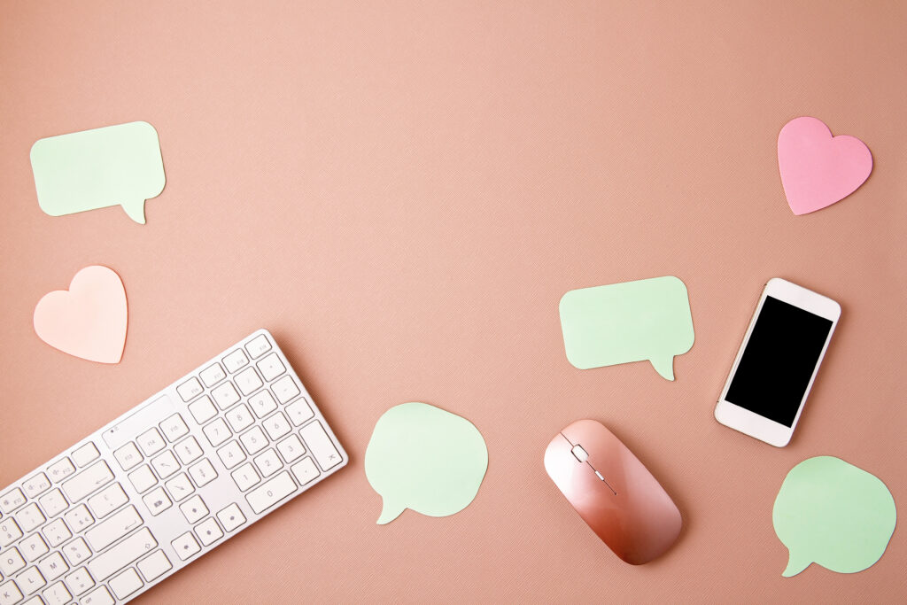 Bureau rose avec clavier, souris, smartphone et bulles de dialogue illustrant la gestion des réseaux sociaux et la communication digitale